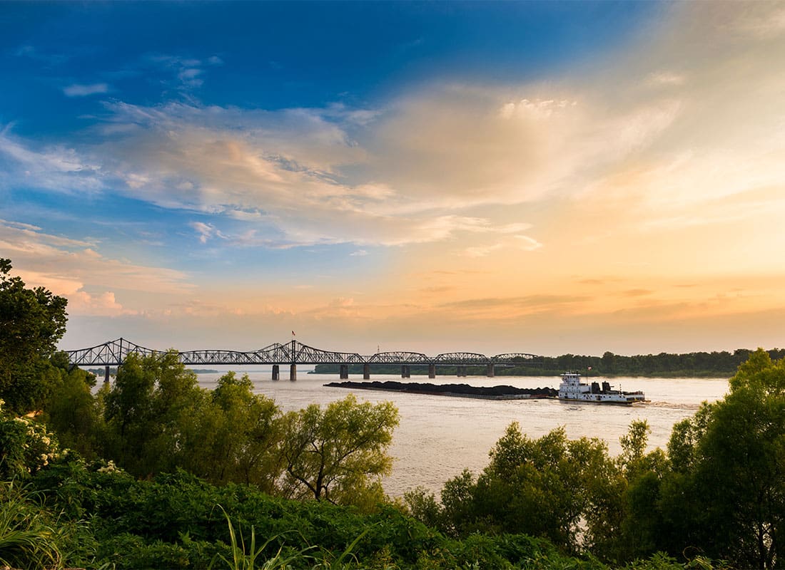 Vicksburg, MS - View of a Bridge with a Boat in the River at Sunset with a Colorful Sky in Vicksburg Mississippi